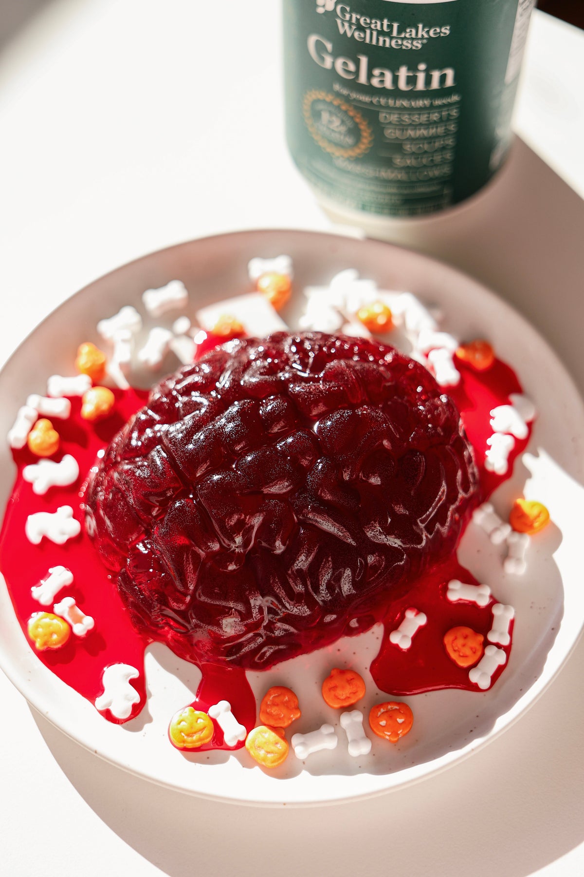 Red brain-shaped gelatin dessert with fake blood and Halloween sprinkles beside a can of Great Lakes Wellness Beef Gelatin.