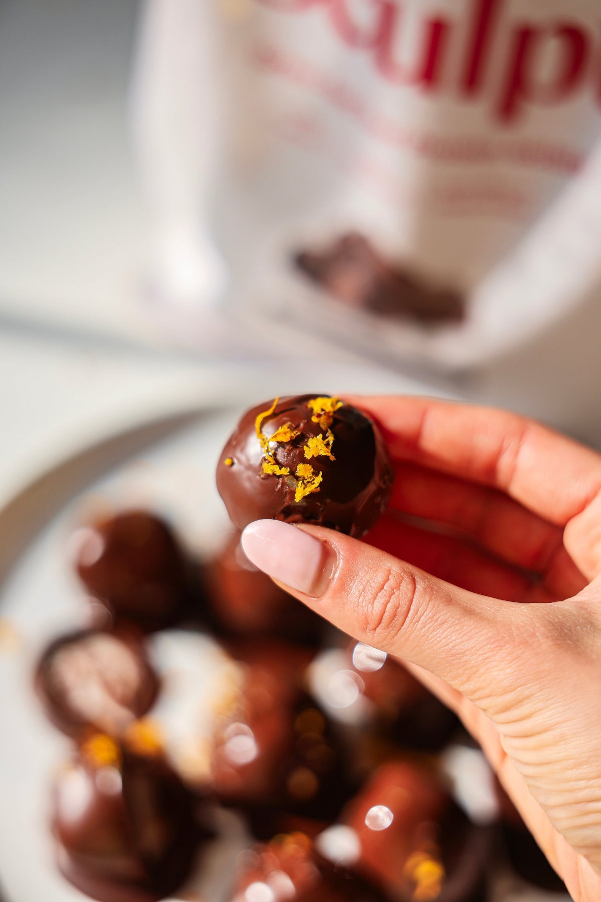 Chocolate-dipped orange protein bite topped with orange zest, with Great Lakes Wellness Sculpt in the background.