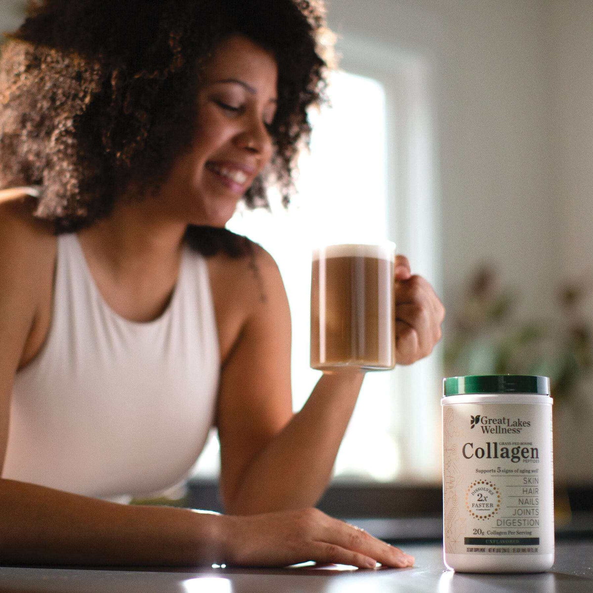 Woman holding coffee near 10oz Collagen Peptides container by Great Lakes Wellness on table