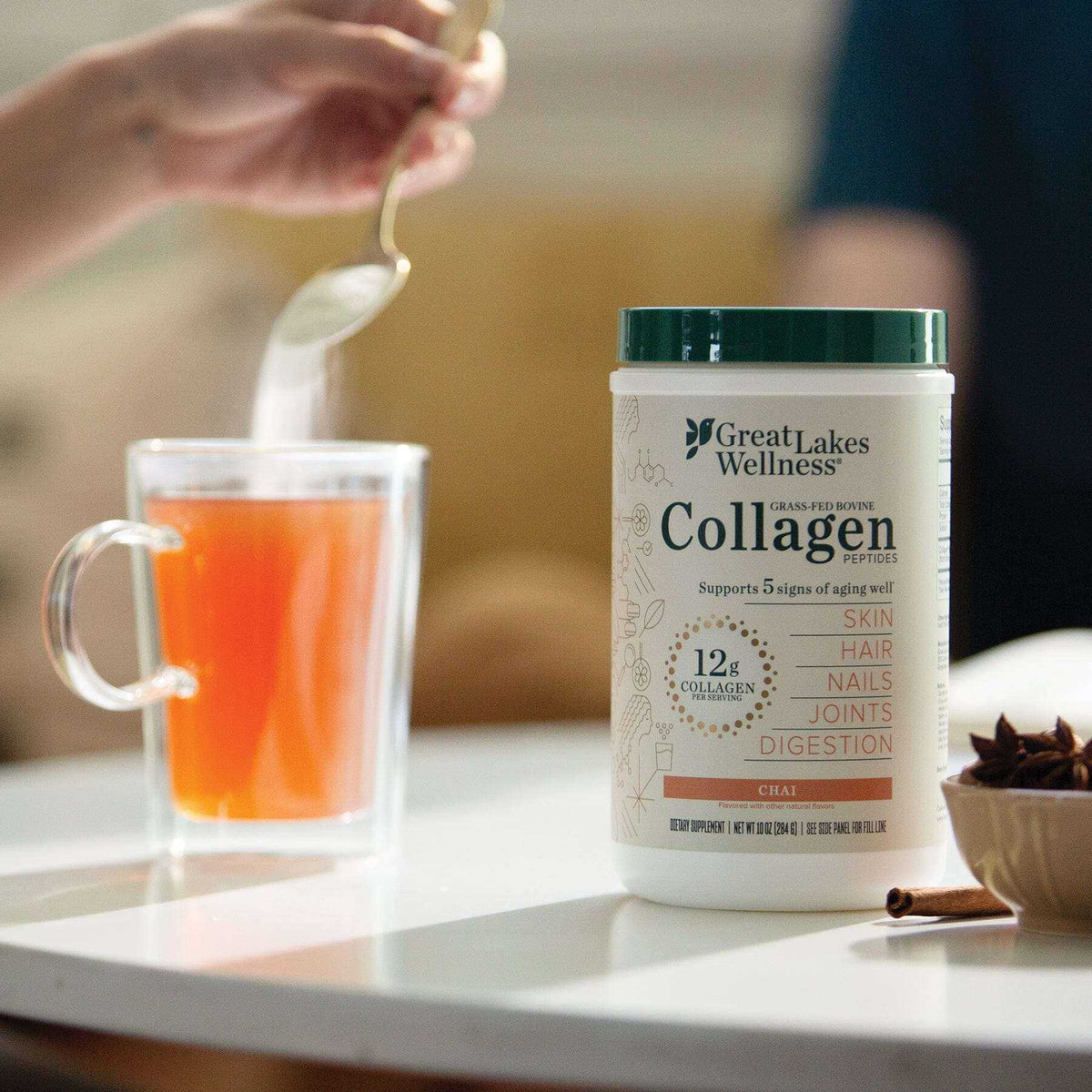 Great Lakes Wellness Chai Collagen Peptides container next to a cup of chai tea with a spoon stirring powder into the drink