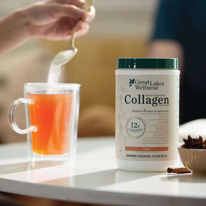 Great Lakes Wellness Chai Collagen Peptides container next to a cup of chai tea with a spoon stirring powder into the drink